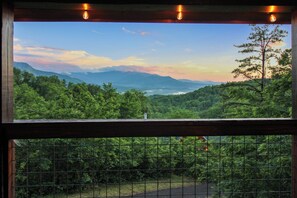 Visão pela janela, com grade de metal, mostrando uma paisagem arborizada e montanhas ao longe.