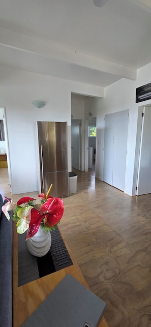 Eine moderne Küche mit einem Edelstahlkühlschrank, ein Essbereich mit Tisch und Stühlen sowie ein Flur zu den Schlafzimmern.