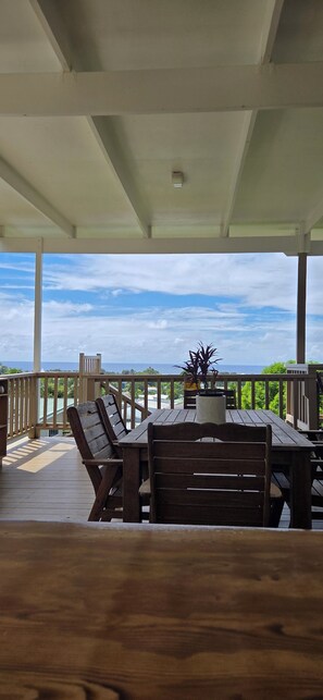 Ein überdachter Außenbereich mit Holztisch und -stühlen, einem Blumentopf und Blick auf das Meer.