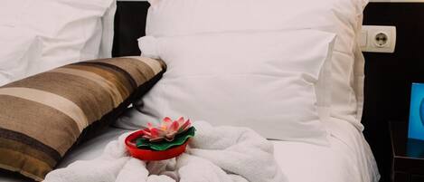 A neatly made bed with white bedding, a striped pillow, and a red decorative item on the bed.