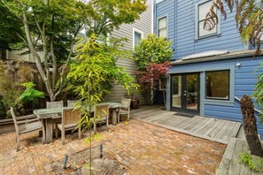 A backyard with a wooden deck, a brick patio, and a blue house. - SF Presidio Heights Haven + Steps 2 Presidio Park (San Francisco)