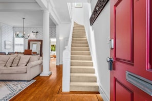 Eine Treppe führt zu einer Empore, einer roten Tür und einem Wohnzimmer mit einem beigefarbenen Sofa.