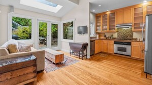 A modern kitchen with wooden cabinets, a built-in oven, and a large window overlooking a garden. - SF Presidio Heights Haven + Steps 2 Presidio Park (San Francisco)
