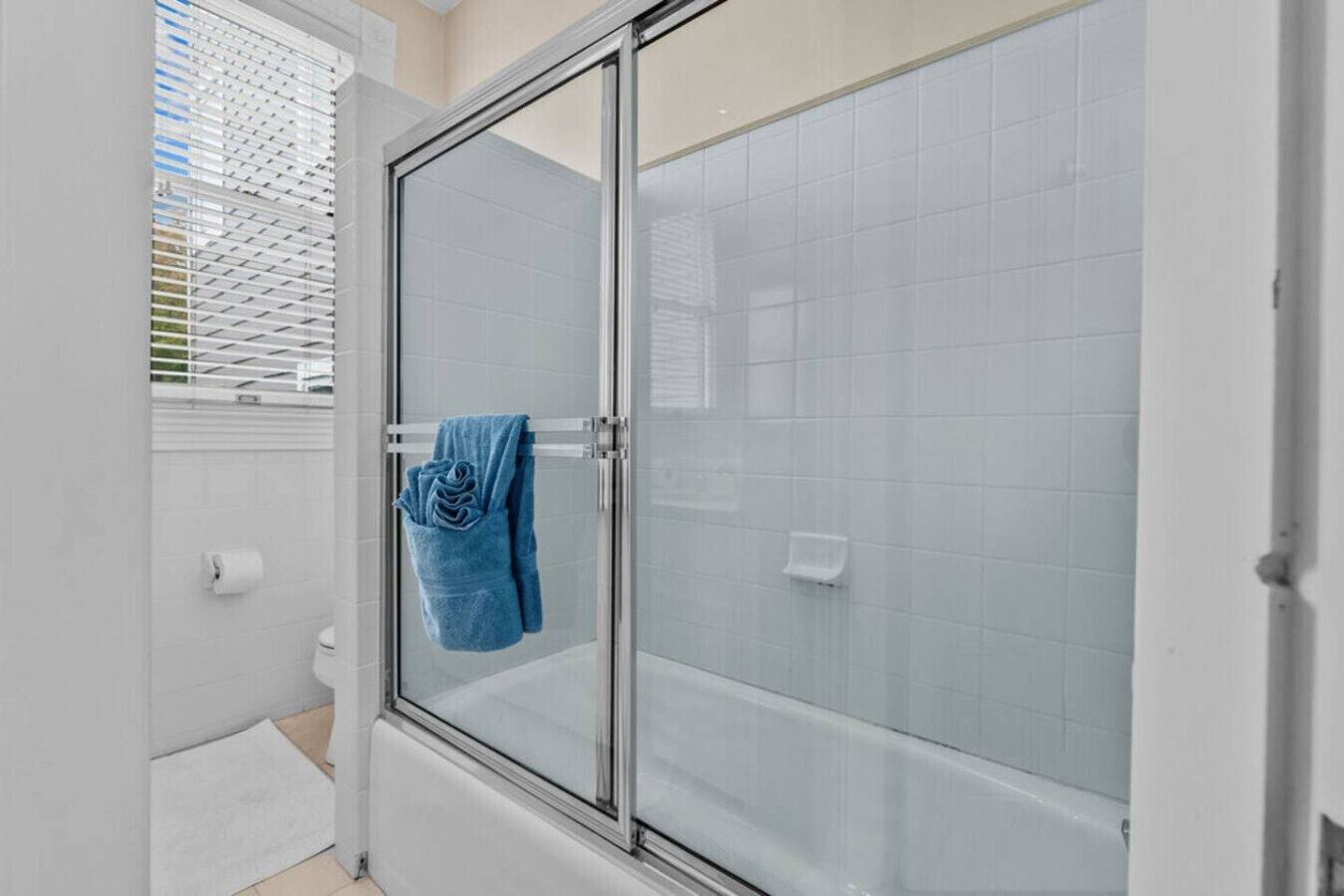 Un baño con cabina de ducha de vidrio, paredes de azulejos blancos y una toalla colgada en la puerta.