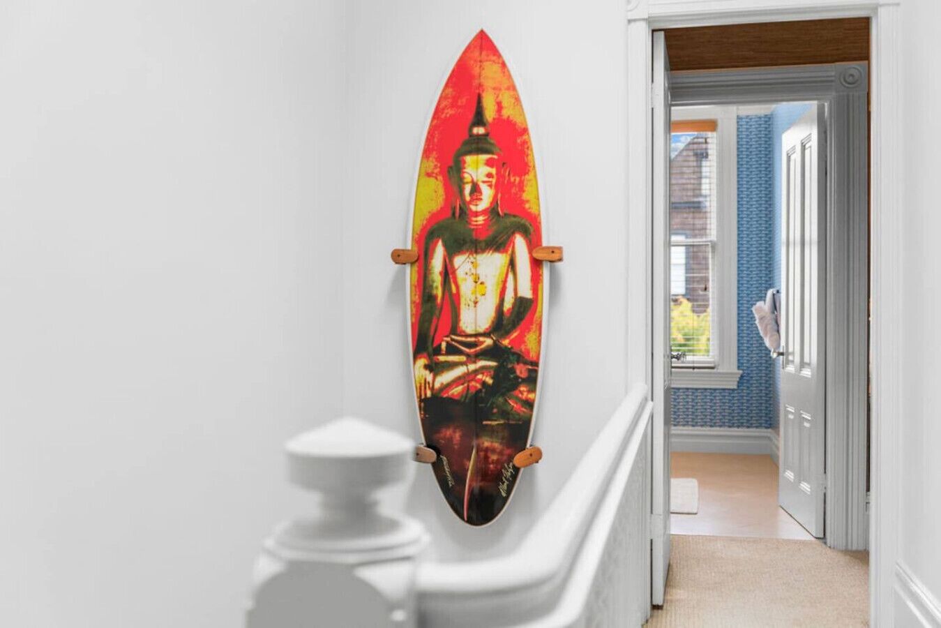 Un pasillo con una obra de arte de tabla de surf, una estatua blanca y una puerta que da a una habitación con pared azul.