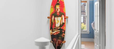 A hallway with a surfboard art piece, a white statue, and a door leading to a room with a blue wall.