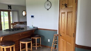 A kitchen with a bar area, wooden stools, a clock, and a door with a sign.