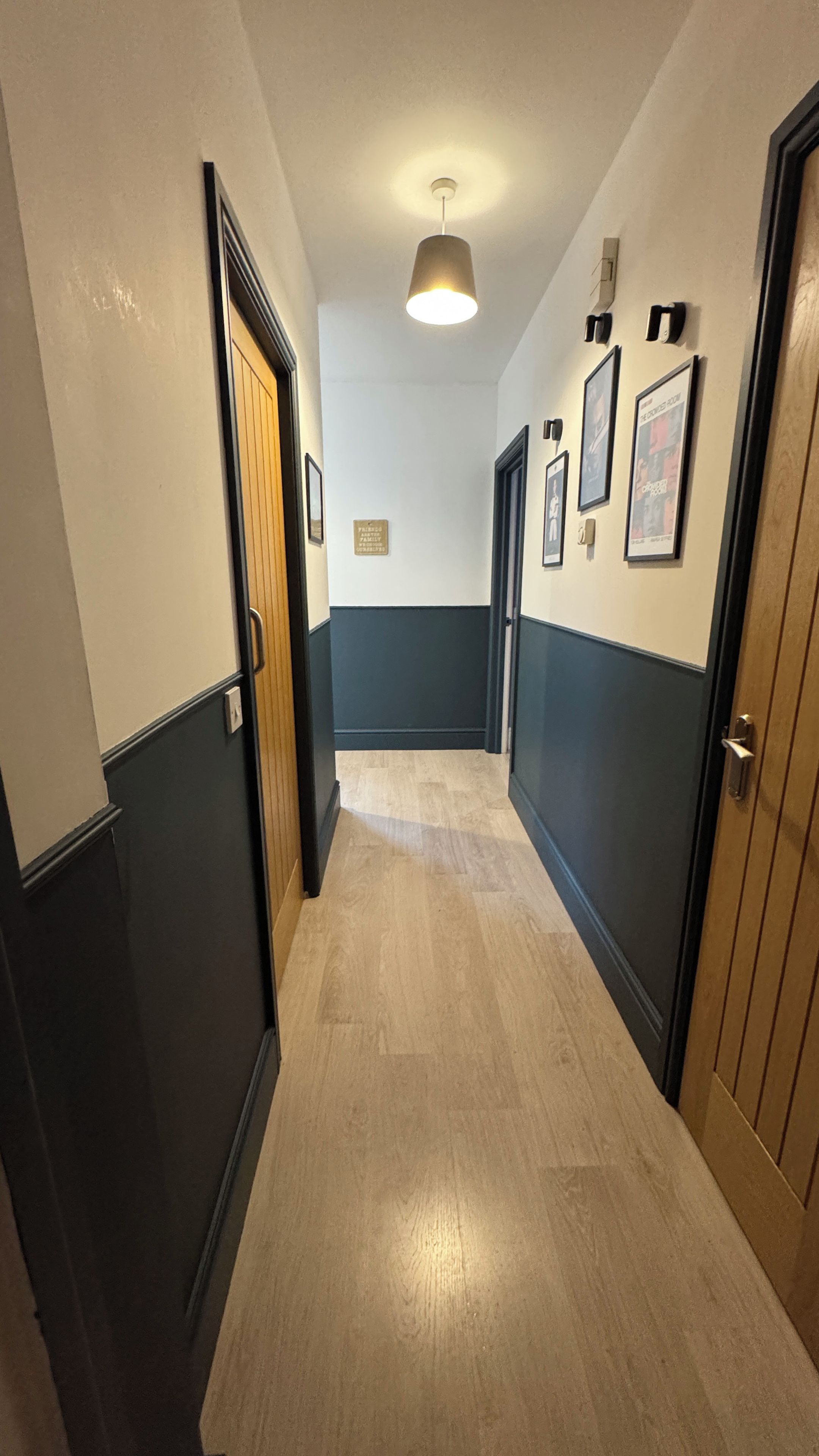 A hallway with doors on both sides, a light fixture on the ceiling, and framed pictures on the walls.