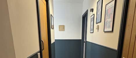 Un couloir avec des portes de part et d’autre, un luminaire au plafond et des tableaux encadrés accrochés aux murs.