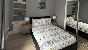 Et soveværelse med en seng, to sengeborde, et spejl og en hylde med pynteting.