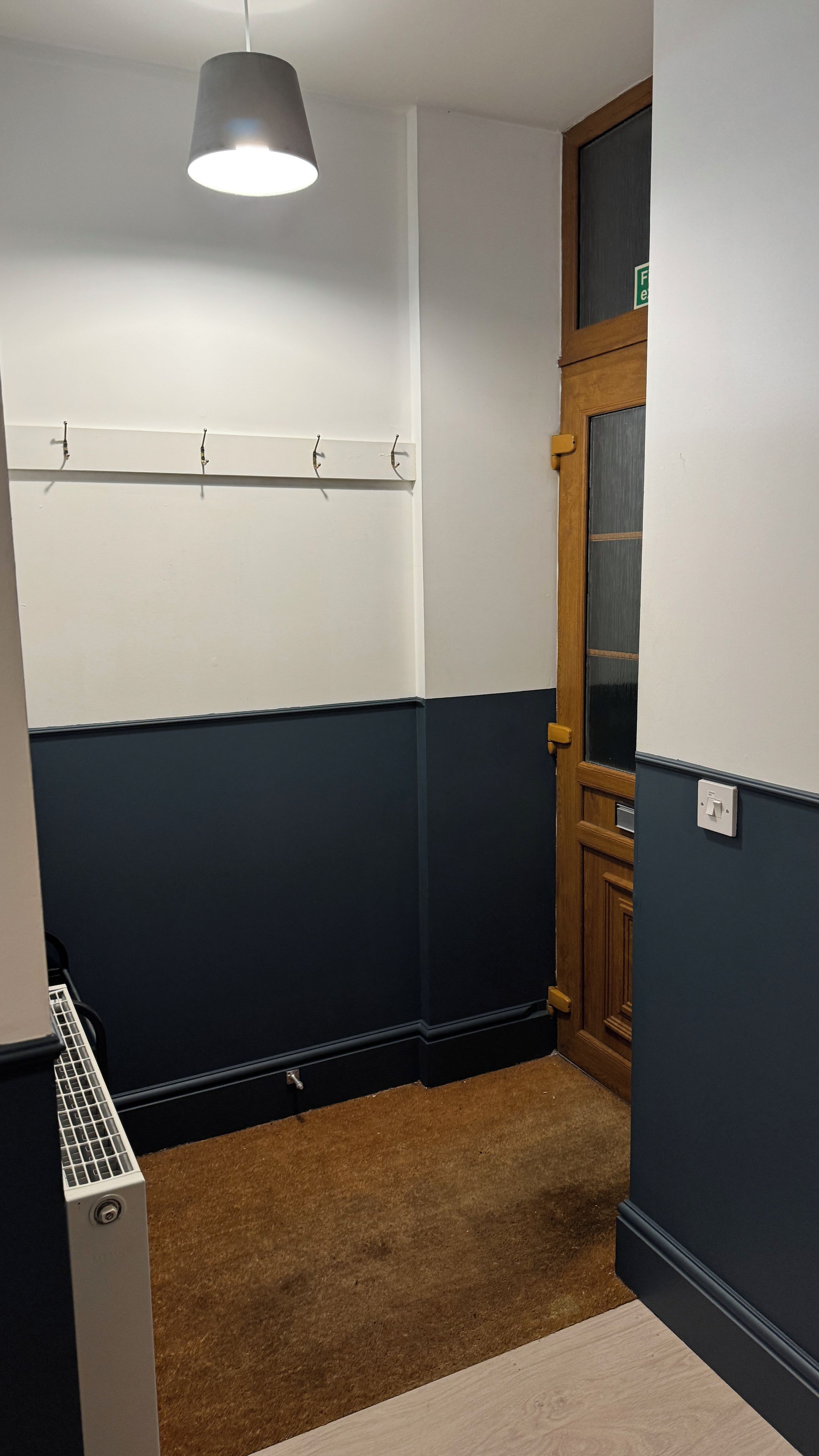 A corner of a room with a coat rack, a door with a glass panel, and a radiator.