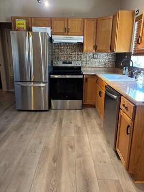 A kitchen with stainless steel appliances, wooden cabinets, a tiled backsplash, and a wooden floor.