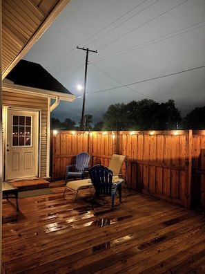 A wooden deck with a covered porch, a white door, and two chairs.