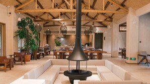 Un espacio interior amplio con una zona de estar central, vigas de madera en el techo e iluminación colgante.