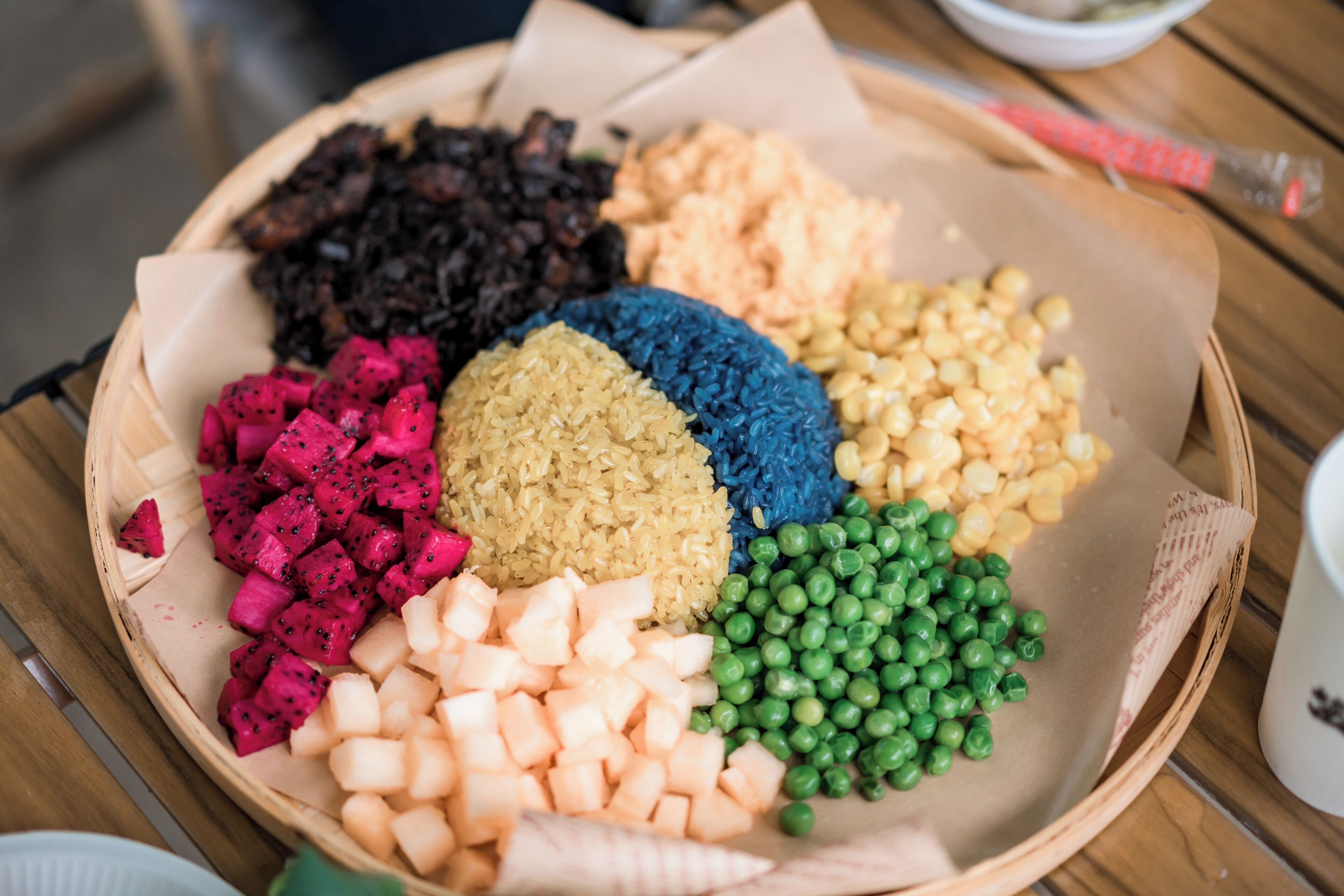 A wooden table with a woven basket containing various food items.