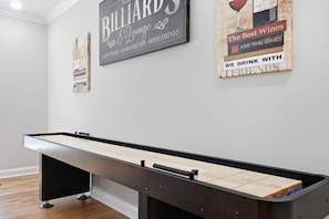 Une table de billard dans une pièce aux murs blancs, avec deux affiches accrochées au mur et un plancher en bois.