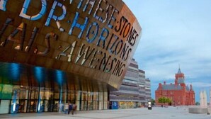 Um edifício moderno com fachada curva e a frase 'THESE STONES ARE THE HORIZONS' em destaque.