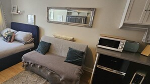 Quarto com cama, sofá, micro-ondas e pequena cozinha.