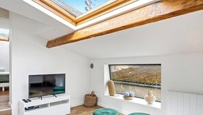 Ein modernes Loft-Schlafzimmer mit Dachfenster, einem Fernseher, einem Fenster mit Blick und einer kleinen Sitzecke.