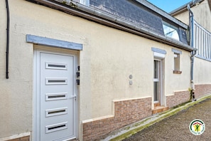 Ein Gebäude mit hellbeiger Fassade, einer weißen Tür mit Lüftungsschlitzen und einem kleinen Fenster.
