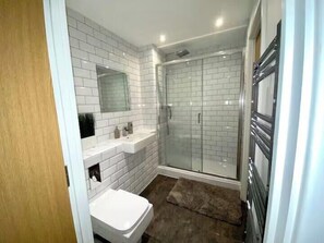 Une salle de bain avec des carreaux de céramique blancs rectangulaires, une douche en verre, un lavabo blanc et une porte en bois.
