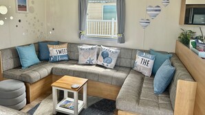 Una sala acogedora con un sofá modular, una mesita de madera y un ventanal con cortinas.