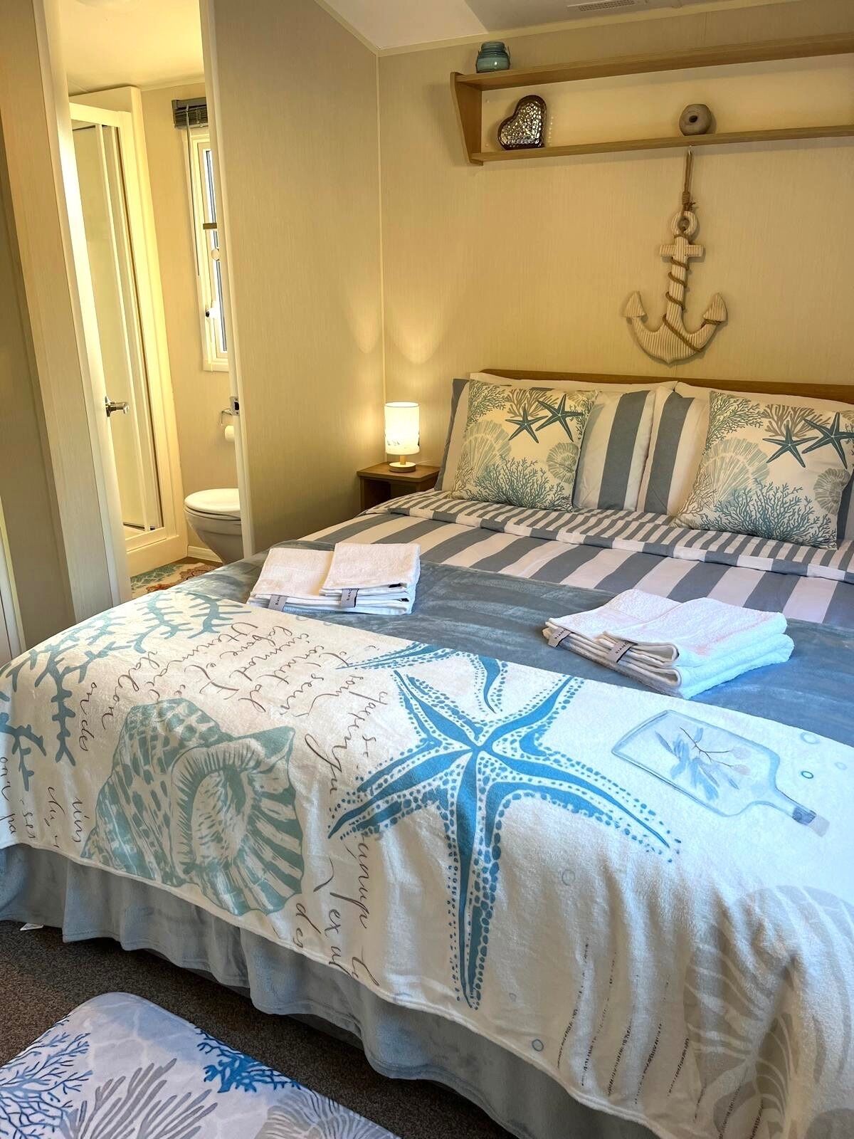A bedroom with a bed, a nightstand, a wall-mounted shelf, and a door leading to a bathroom.