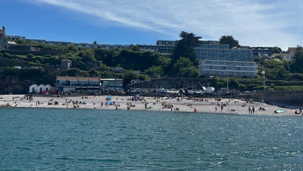 Una playa costera con un muro de piedra, sombrillas de playa y gente.