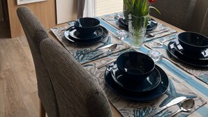 Un comedor con una mesa preparada para cuatro personas, un jarrón de tulipanes y vistas a un balcón con barandilla.