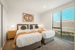 Ein modernes Schlafzimmer mit zwei Betten, einem großen Fenster mit Jalousien und einem einzigartigen Wandbild.