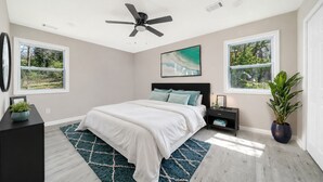 A bedroom with a bed, a ceiling fan, two windows, a nightstand, a dresser, and a potted plant. - New Renovated 3BD-2BA Home • Minutes to Mercedes Benz, Midtown and Beltline (Atlanta)