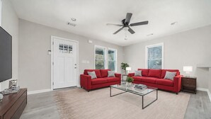 A living room with two red sofas, a glass coffee table, a ceiling fan, and a door with a window. - New Renovated 3BD-2BA Home • Minutes to Mercedes Benz, Midtown and Beltline (Atlanta)