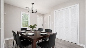 A dining room with a rectangular table, black chairs, a vase with green plants, and a chandelier. - New Renovated 3BD-2BA Home • Minutes to Mercedes Benz, Midtown and Beltline (Atlanta)
