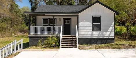 A single-story house with a front porch, a small staircase leading to the door, and a front yard.