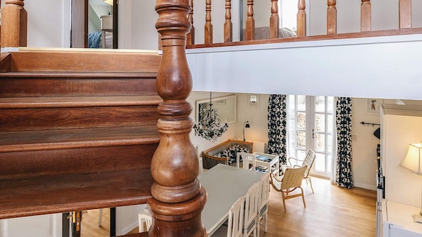 Una escalera de madera con barandilla que lleva a un área en el segundo piso con una mesa y sillas de comedor.
