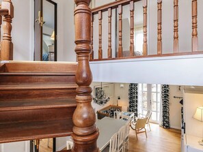 A wooden staircase with a balustrade leading to a second-floor area with a dining table and chairs.