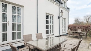 Un edificio blanco con ventanas amplias y una mesa de vidrio con sillas de mimbre.