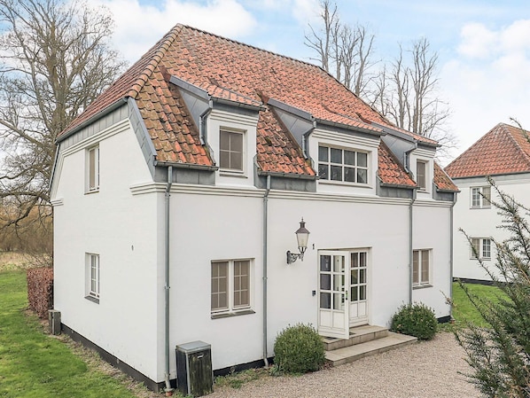 A two-story house with a red-tiled roof, white exterior walls, and a front door with a small porch.