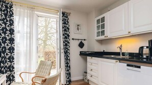 Una cocina con armarios blancos, encimera negra y una ventana con cortinas ligeras.