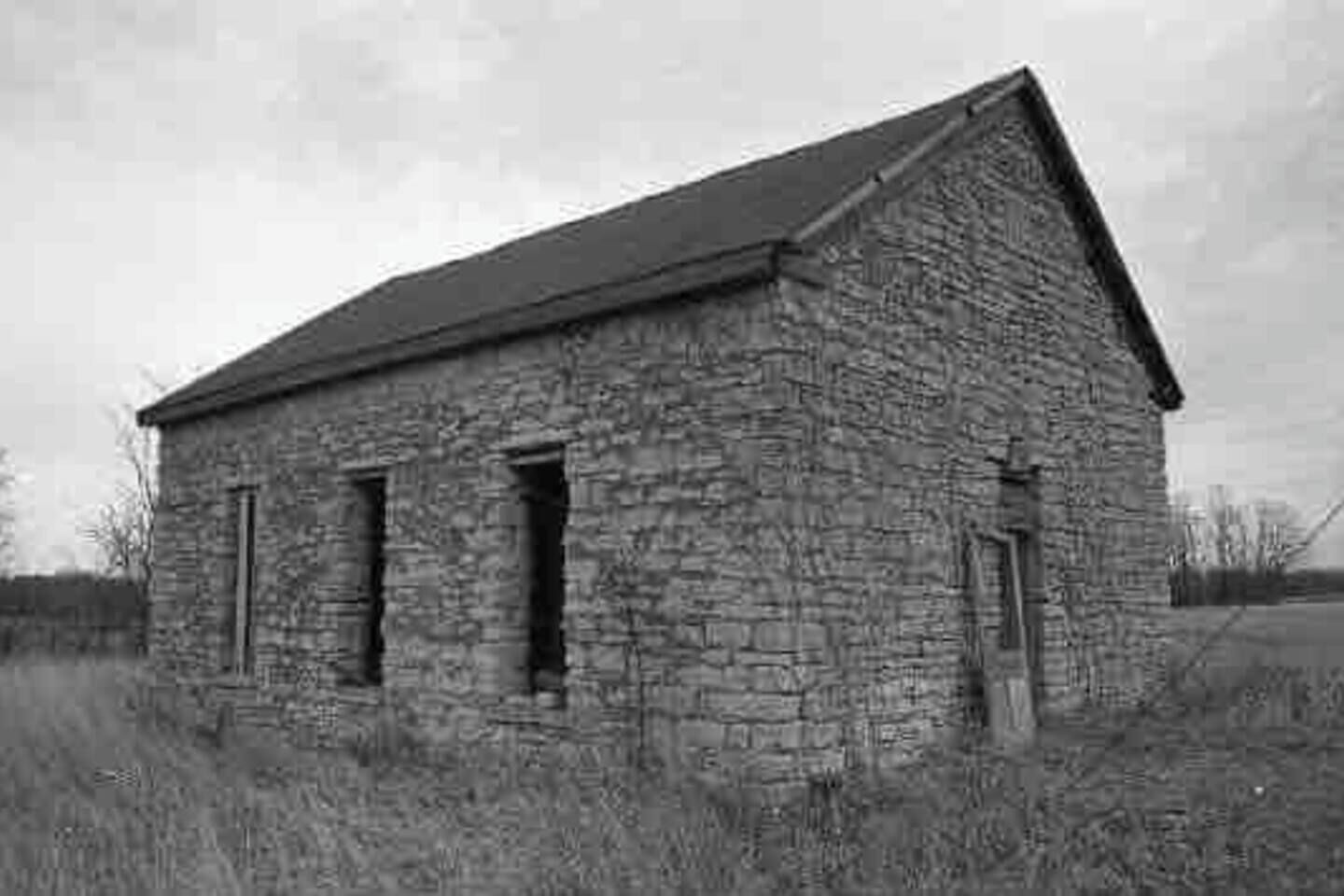 A stone building with a gabled roof, two windows, and a door.