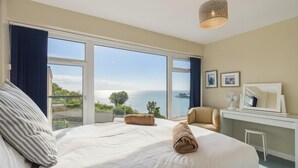 A hotel room with a large bed, a chair, a desk with a mirror, and a view of the sea. - Golwg y Môr - 2 Bedroom Apartment - Tenby (Tenby)