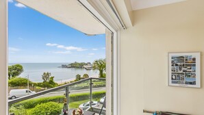 A balcony with a view of the sea, a framed collage on the wall, and a table with a bottle and glasses. - Golwg y Môr - 2 Bedroom Apartment - Tenby (Tenby)