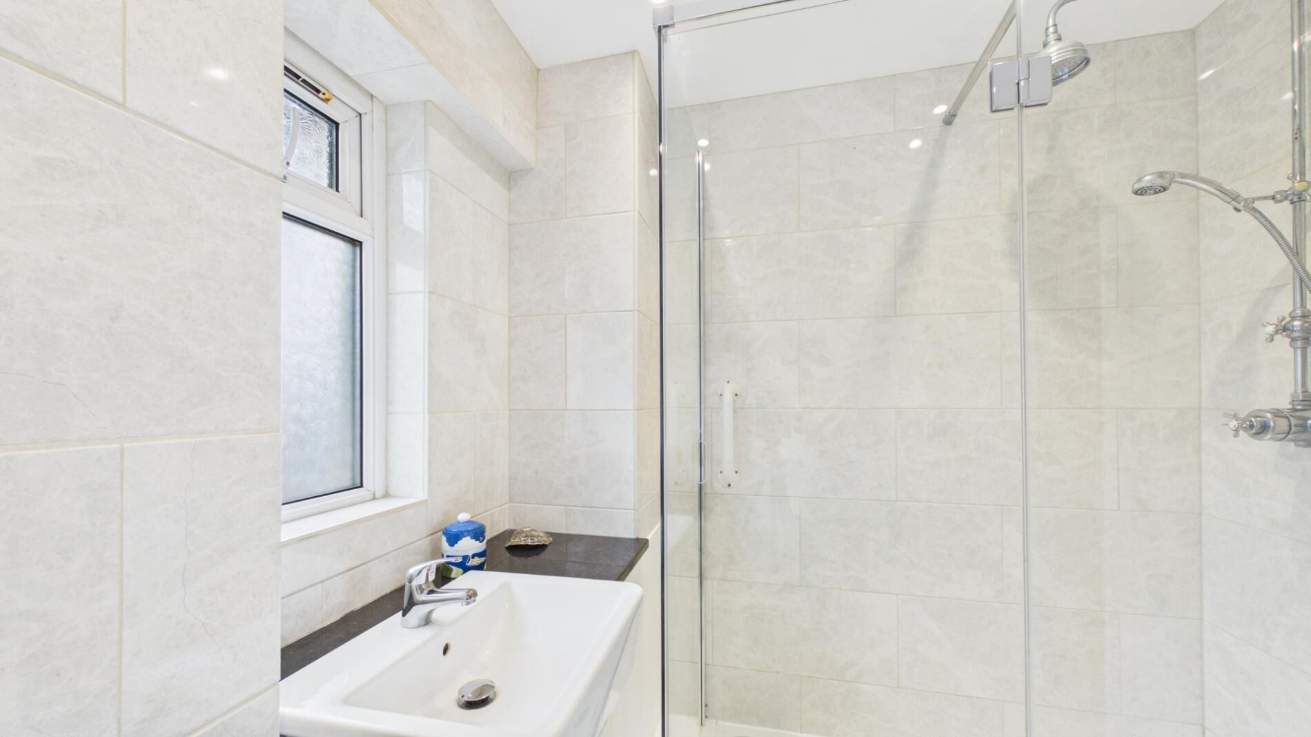 A modern bathroom with a glass shower enclosure, a sink with a mirror, and a window above the sink.