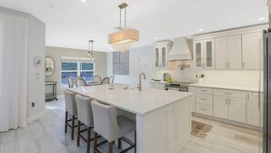 A modern kitchen with a large island, white cabinetry, and pendant lighting. - 3BR 3BA House - Pool & Spa - Beach Access Included (Marco Island)