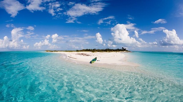 Ein Strand mit klarem türkisblauem Wasser, einem Sandufer und einer kleinen Insel mit Vegetation in der Ferne.