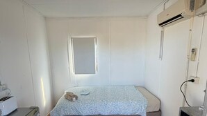 Een kleine kamer met een enkel bed, een raam, een kitchenette en een houten vloer.