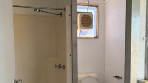 Een badkamer met een bad, toilet en een raam met een airconditioning.