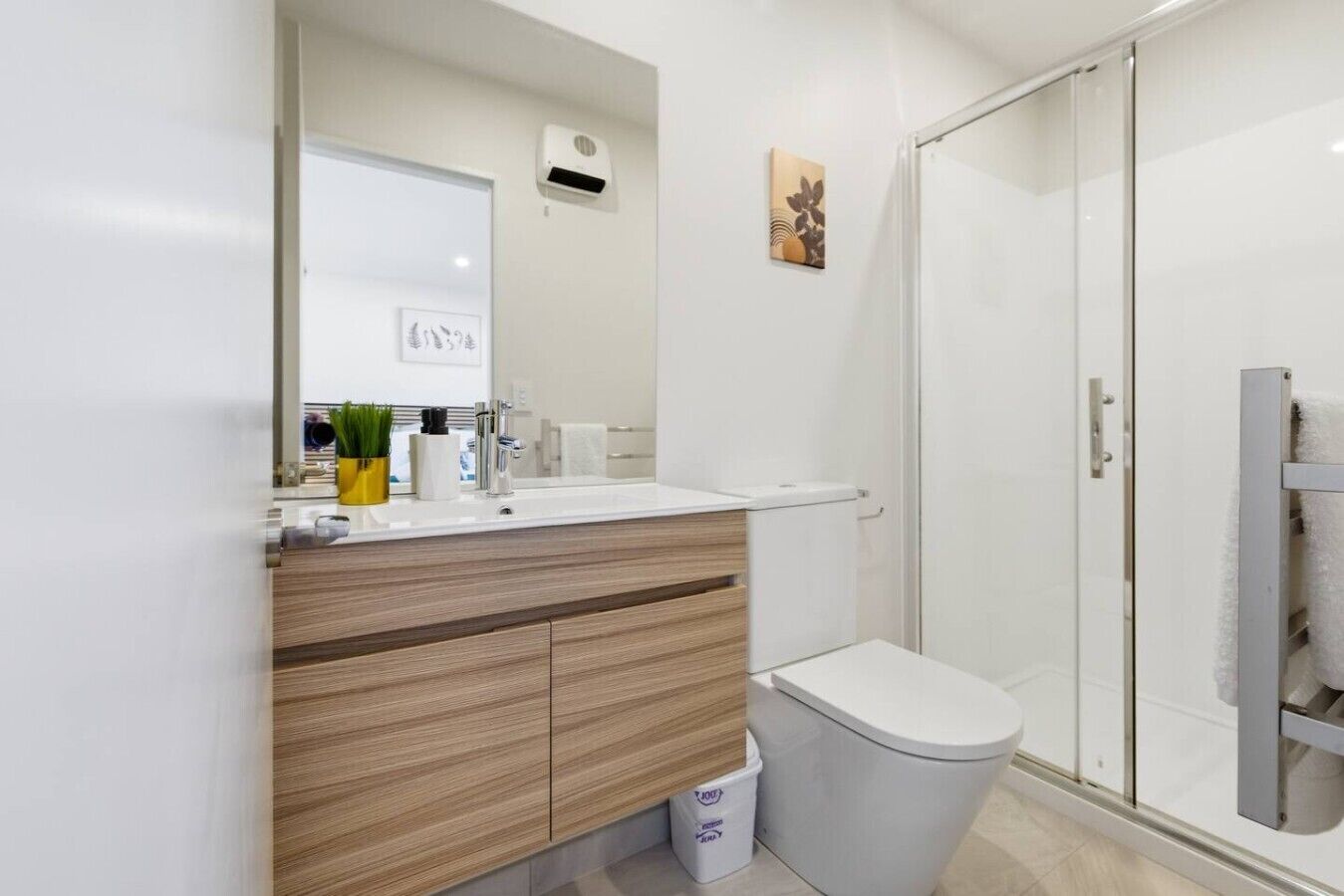 A modern bathroom with a white sink, wooden vanity, toilet, and a glass shower enclosure.