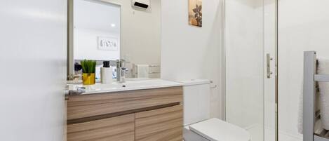 A modern bathroom with a white sink, wooden vanity, toilet, and a glass shower enclosure.