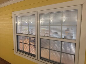 Ein Fenster mit Jalousien, eine gelbe Wand und eine sichtbare Backsteinmauer draußen.